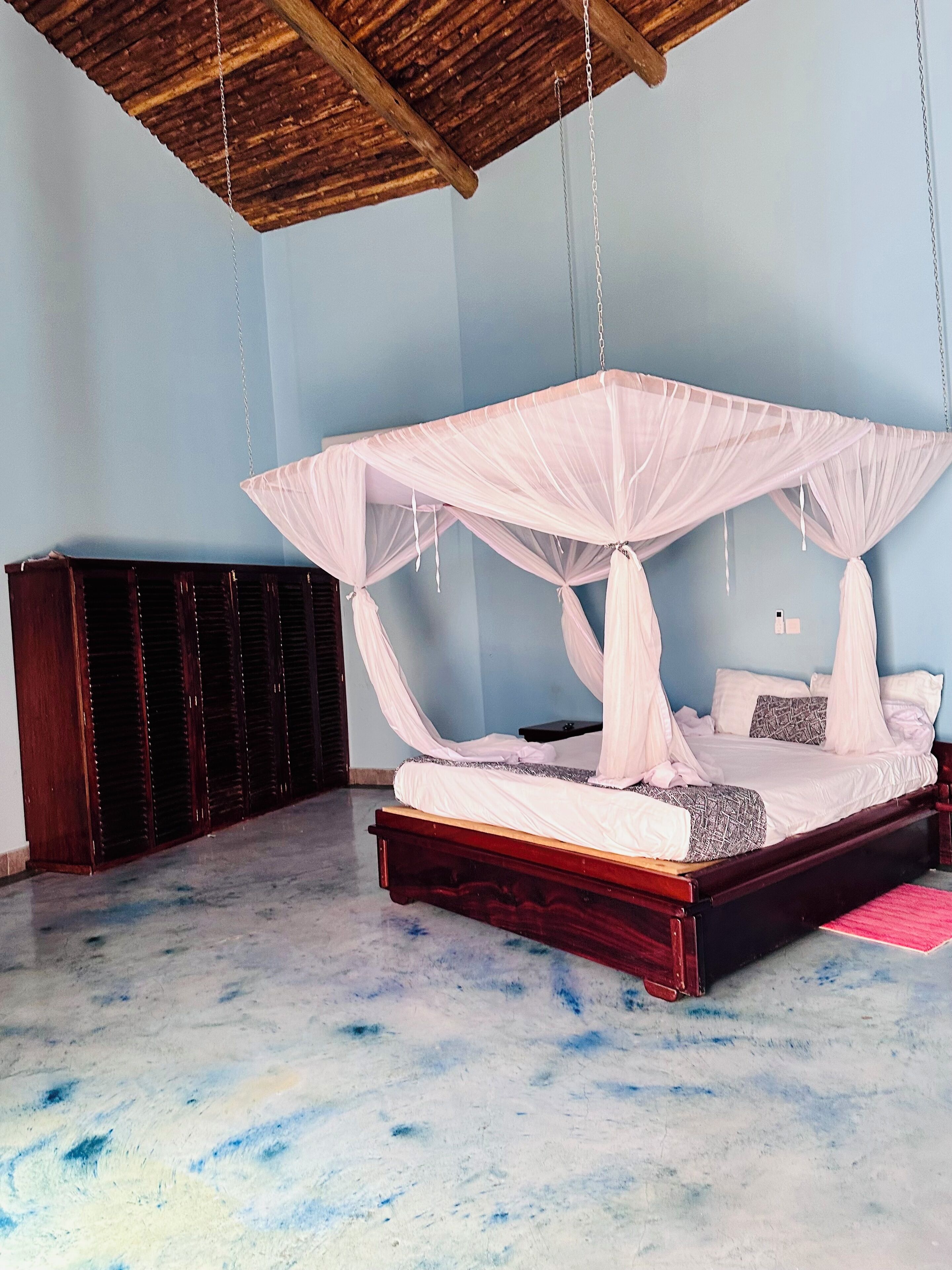 Une chambre à coucher avec un lit sous un dais, une armoire en bois et un plancher en béton.