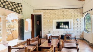 A spacious dining area with wooden tables and benches, a brick wall, and a large flat-screen TV mounted on the wall. - Villa Jahawi (Diani Beach)