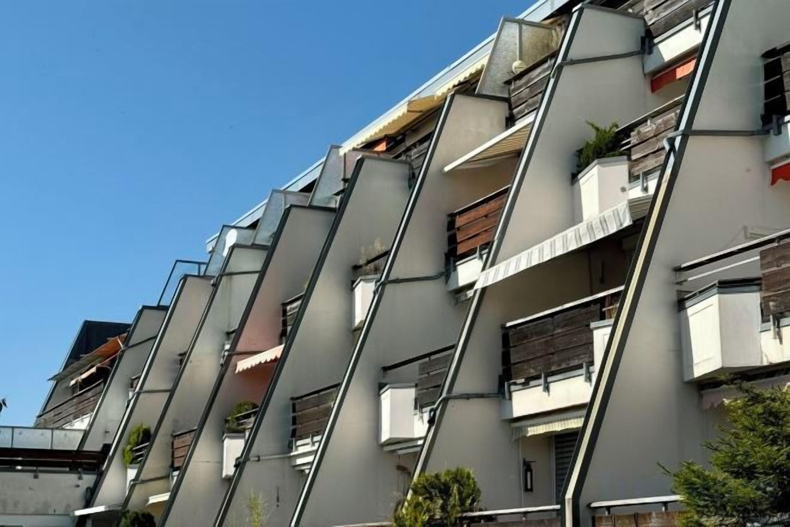 Edifício residencial com várias andares e varandas, algumas com plantas.