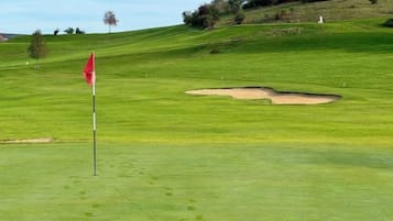 Campo de golfe com haste de sinalização, bunker de areia e colinas verdes onduladas.