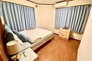 A bedroom with a bed, a bedside table with a lamp, a dresser, and a window with curtains. - 4 bedrooms, 2 bathrooms, 2 toilets, spacious house with convenient transportation (Kyoto)