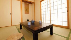 Une pièce de style japonais traditionnel, avec un sol recouvert de tatamis, une petite table basse sur laquelle est disposé un service à thé, des portes coulissantes et une grande fenêtre.