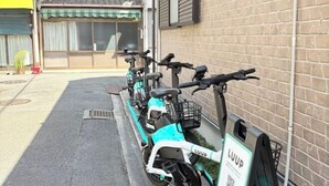 Une rangée de trottinettes électriques est garée contre un mur de briques, avec un code QR pour le service LUUP.
