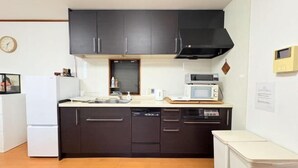 Une cuisine de taille réduite, avec des meubles de couleur sombre, un réfrigérateur blanc, un four à micro-ondes et un lave-vaisselle.