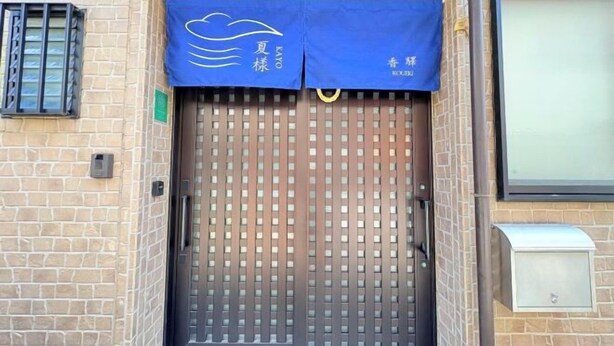 L’entrée d’un hôtel, avec un portail en métal, un auvent bleu orné de caractères chinois et un mur de briques.