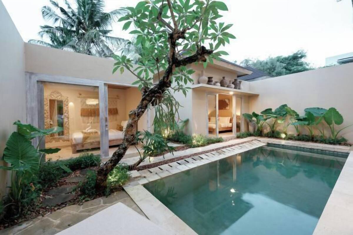 A modern poolside area with a clear pool, a tree, and a building with glass doors and a visible interior.