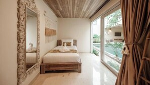 A bedroom with a wooden ceiling, a large mirror, a bed with white bedding, and a view of greenery outside. - Sapta Villa Ubud (Bali)
