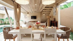 A dining area with a wooden table and chairs, a chandelier, and a staircase in the background. - Sapta Villa Ubud (Bali)