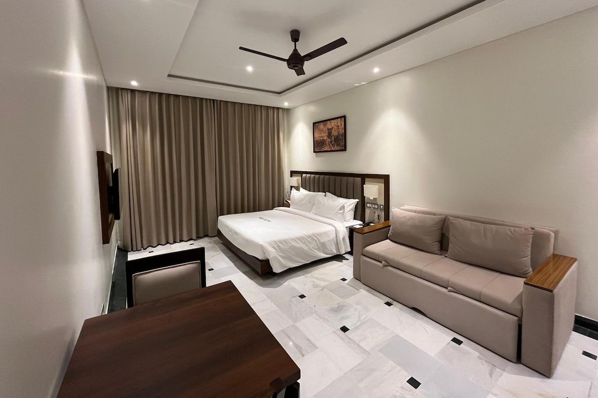 A modern hotel room with a bed, a sofa, a desk, and a ceiling fan.