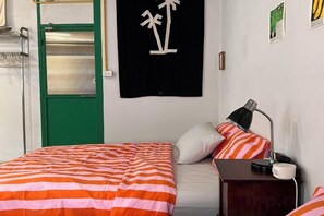 A room with a bed, a desk, a lamp, and a green door. - The Urbanists BKK (Bangkok)