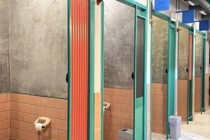 A row of public restroom stalls with tiled walls and a trash bin. - The Urbanists BKK (Bangkok)