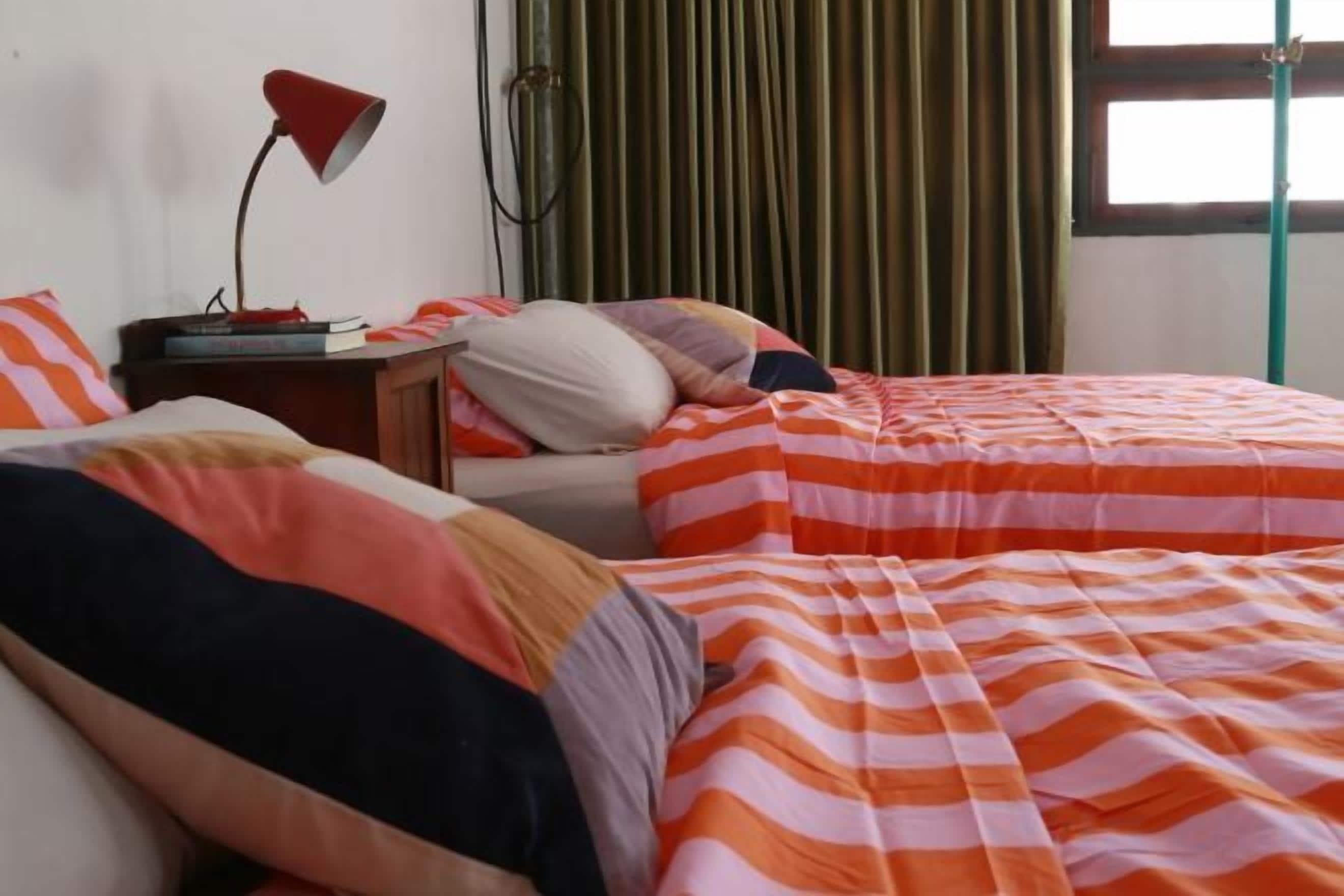 A bedroom with two beds, a nightstand, a lamp, and a window with curtains.