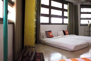 A room with a bed, a window with curtains, and a yellow wall. - The Urbanists BKK (Bangkok)
