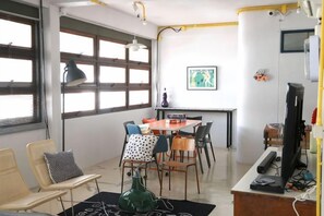 A room with a dining table, chairs, a television, and a window with blinds. - The Urbanists BKK (Bangkok)