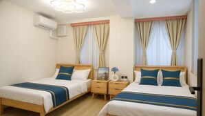 A hotel room with two beds, wooden headboards, beige curtains, a nightstand with a vase, and an air conditioning unit. - sakuranoyado2 (Tokyo)