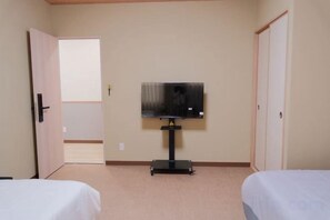 A hotel room with a bed, a television on a stand, and a door leading to another room. - sakuranoyado2 (Tokyo)