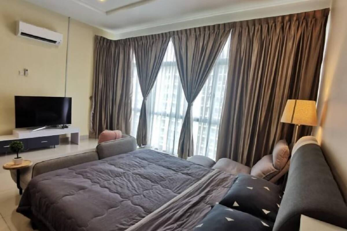 A modern hotel room with a large bed, a flat-screen TV, a small side table, and a window with curtains.
