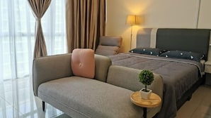 A modern hotel room with a sofa, a bed with a dark headboard, a bedside lamp, and a small potted plant. - Palazio Studio Mount Austin Toppen Ikea by JYNest Johor (Johor Bahru)