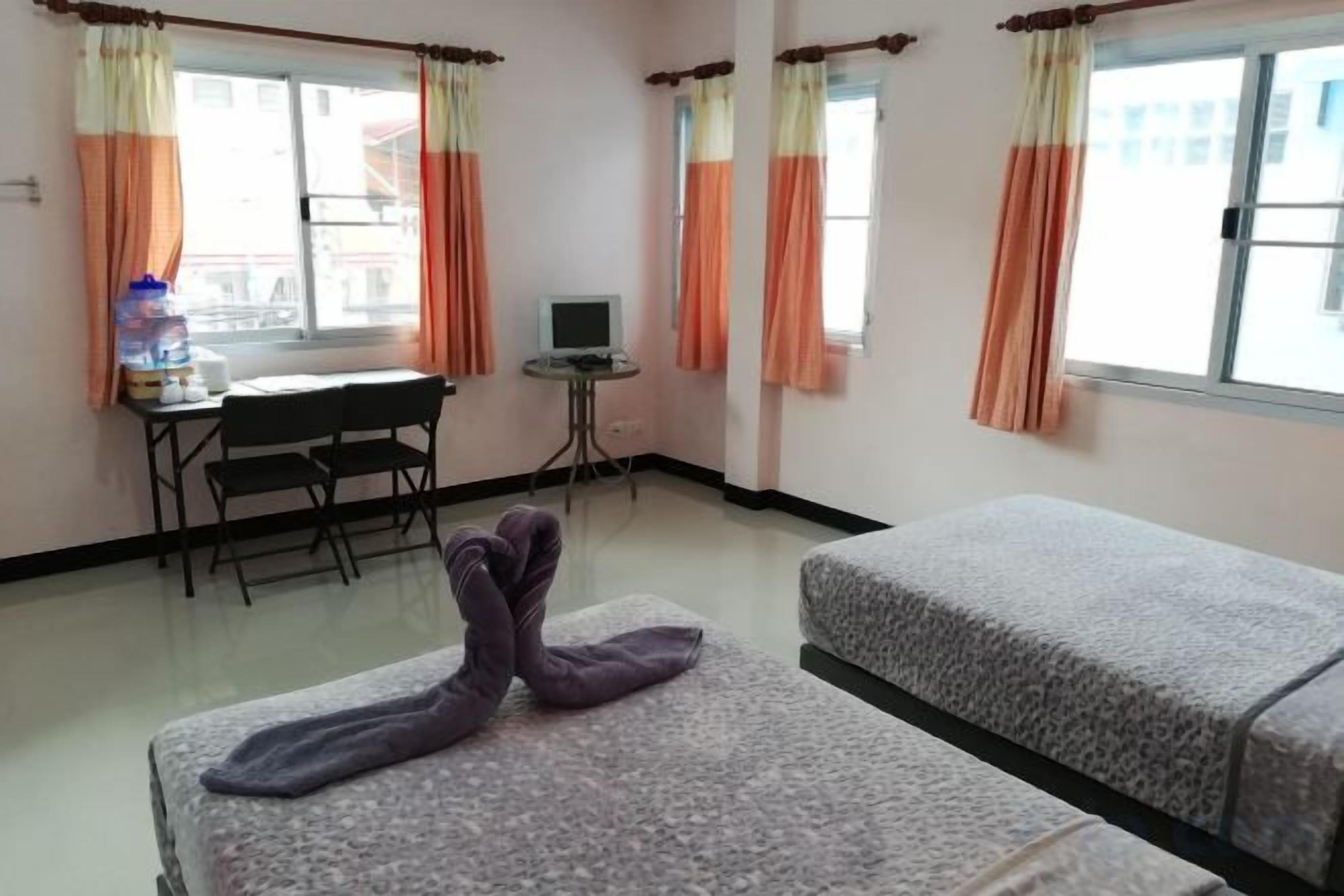 Une chambre d’hôtel avec deux lits, un bureau avec une chaise, une petite table et des rideaux.