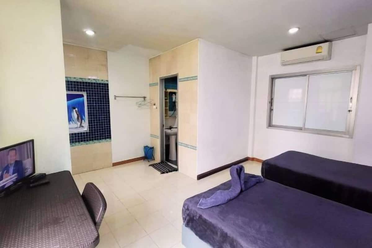 A hotel room with a bed, a desk with a computer, a TV, a bathroom with a shower, and a window.