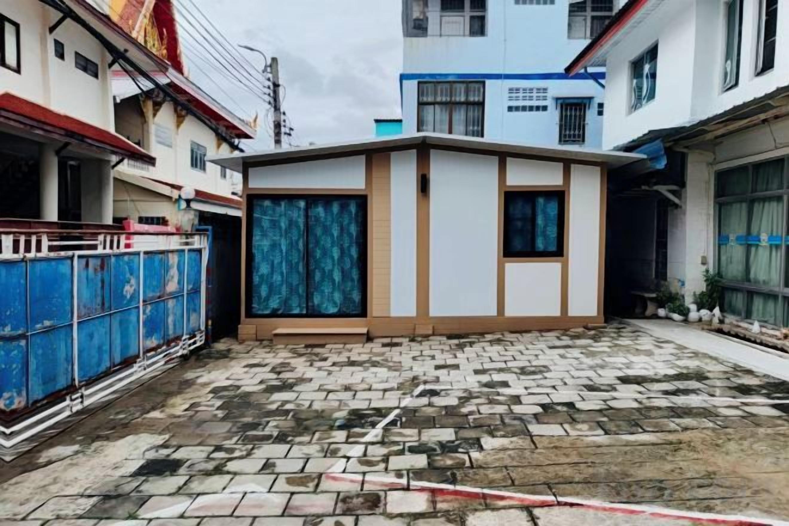 A courtyard with a small building, a blue fence, and a paved ground.