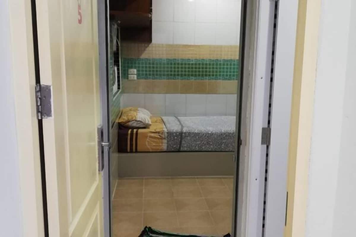 A narrow hallway leading to a room with a bed, a pillow, and a suitcase.