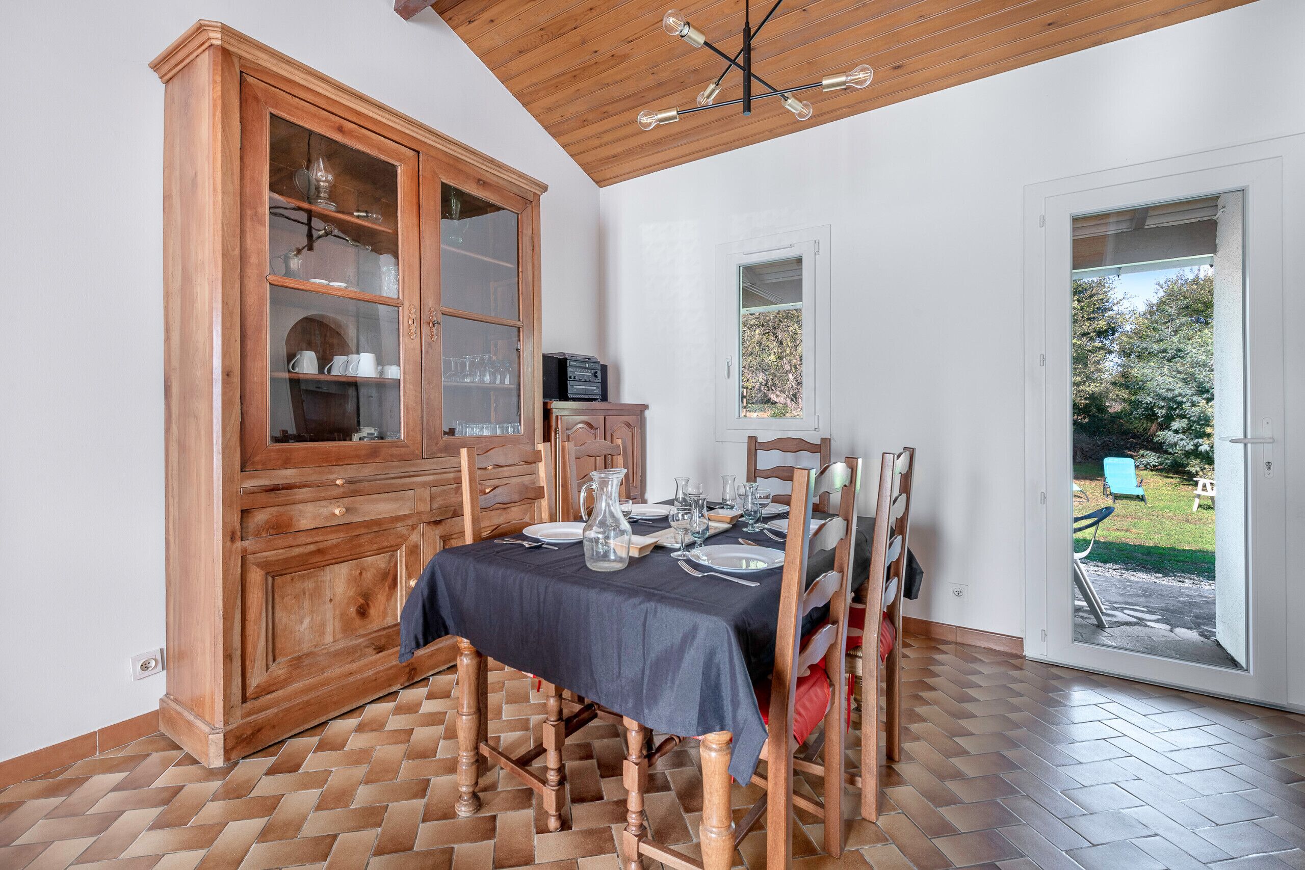 Un coin repas avec un buffet en bois, une table dressée pour quatre personnes et une vue sur l’extérieur grâce à une porte vitrée.