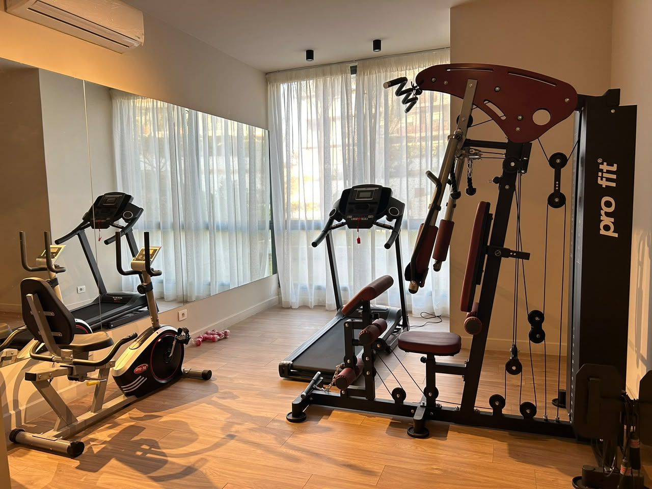 Ein Heimfitnessraum mit Trainingsgeräten, darunter ein Laufband, ein Crosstrainer und eine Gewichtbank.