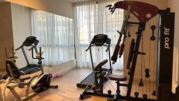 Ein Heimfitnessraum mit Trainingsgeräten, darunter ein Laufband, ein Crosstrainer und eine Gewichtbank.