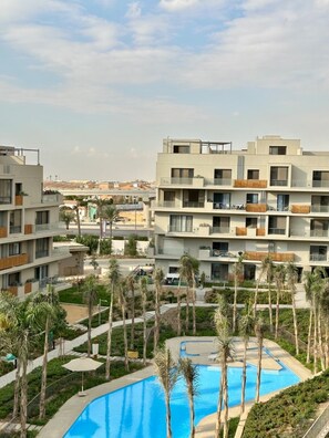 A modern hotel with multiple floors, a swimming pool, and palm trees. - Sodic Villette New Cairo by BirdNest (New Cairo)