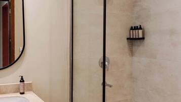 A bathroom with a glass-enclosed shower, a sink with a mirror, and a shelf with toiletries.