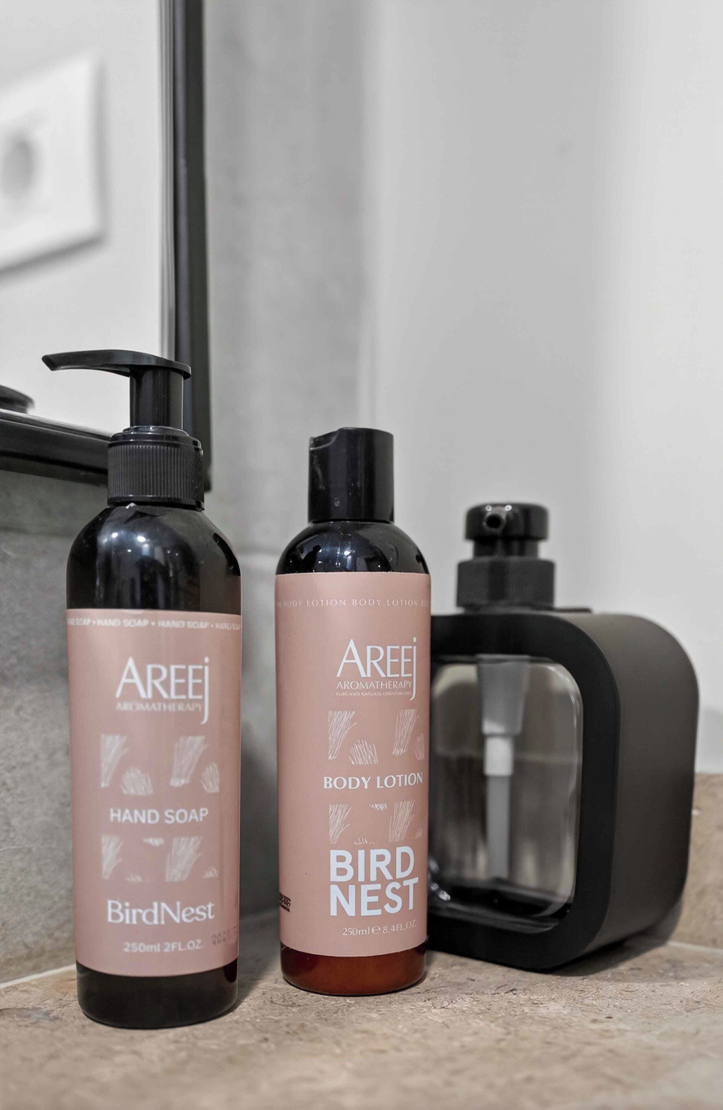 Dos botellas de jabón de manos y loción corporal Areej BirdNest sobre una encimera de baño.