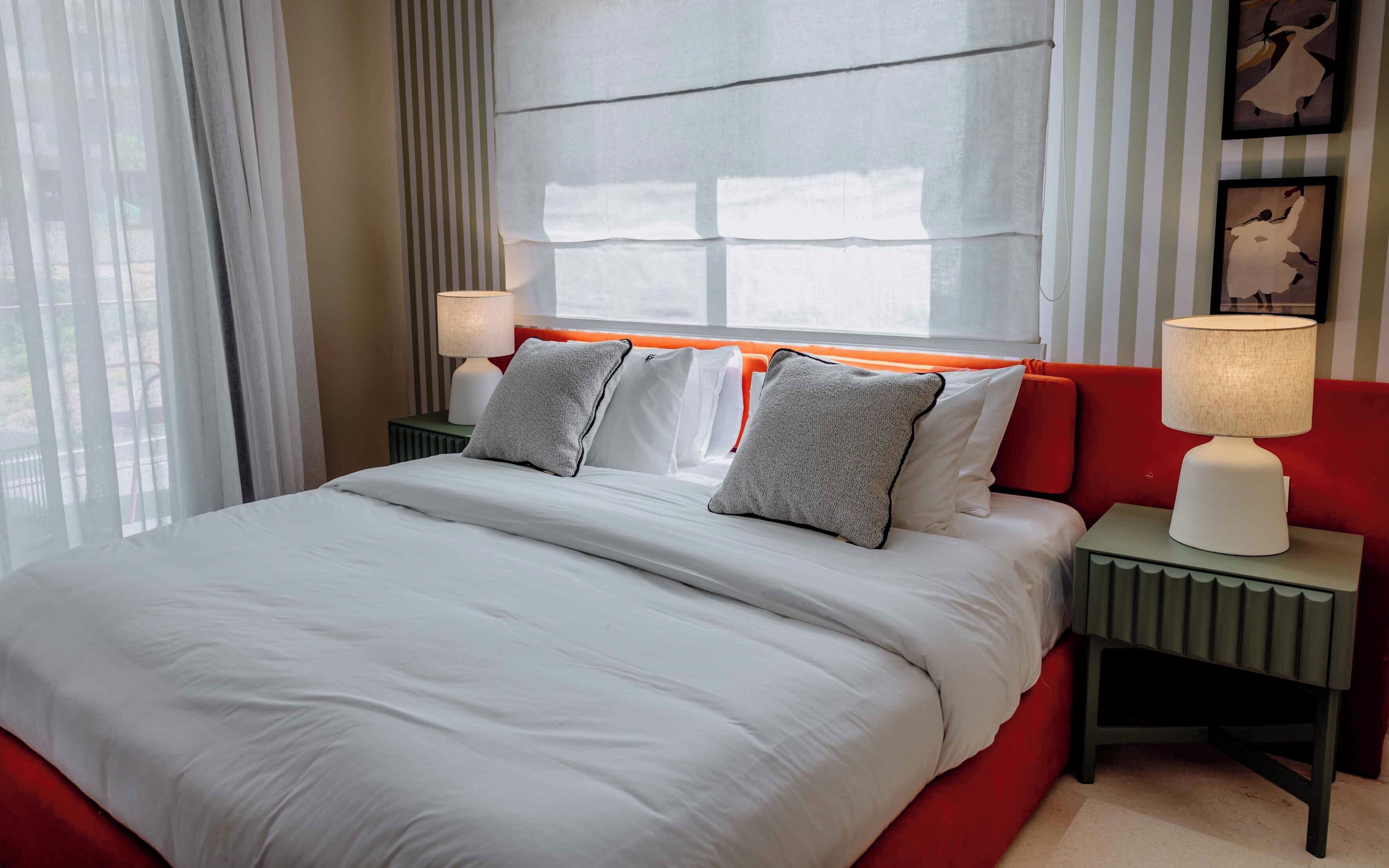 Una camera d'hotel con un letto grande, due comodini, una finestra con tende e opere d'arte alle pareti.