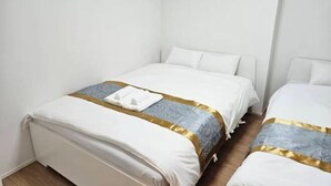 A hotel room with two beds, white bedding, and a gold and blue patterned bedspread. - Yahiro 6chome (Tokyo)