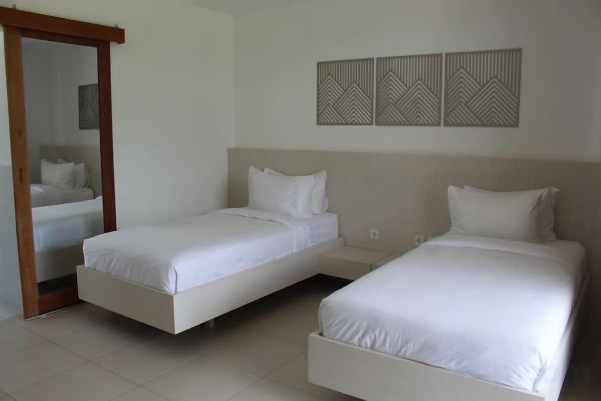 A hotel room with two single beds, a wooden door, a mirror, and a wall with decorative panels.