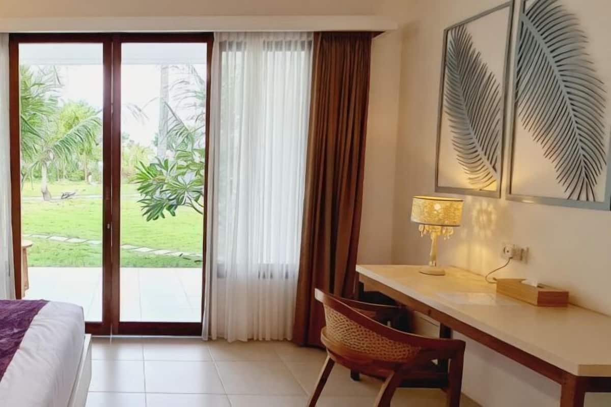 Une chambre d’hôtel équipée d’un lit, d’un bureau, d’une chaise, d’une lampe et offrant une vue sur un jardin grâce à une porte coulissante.