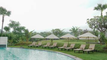 A poolside area with lounge chairs and umbrellas, surrounded by greenery.