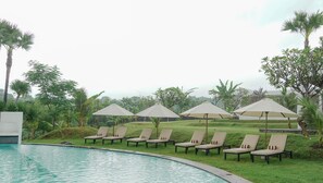 A poolside area with lounge chairs and umbrellas, surrounded by greenery. - Palm Springs Bali Dive Resorts (Tulamben)