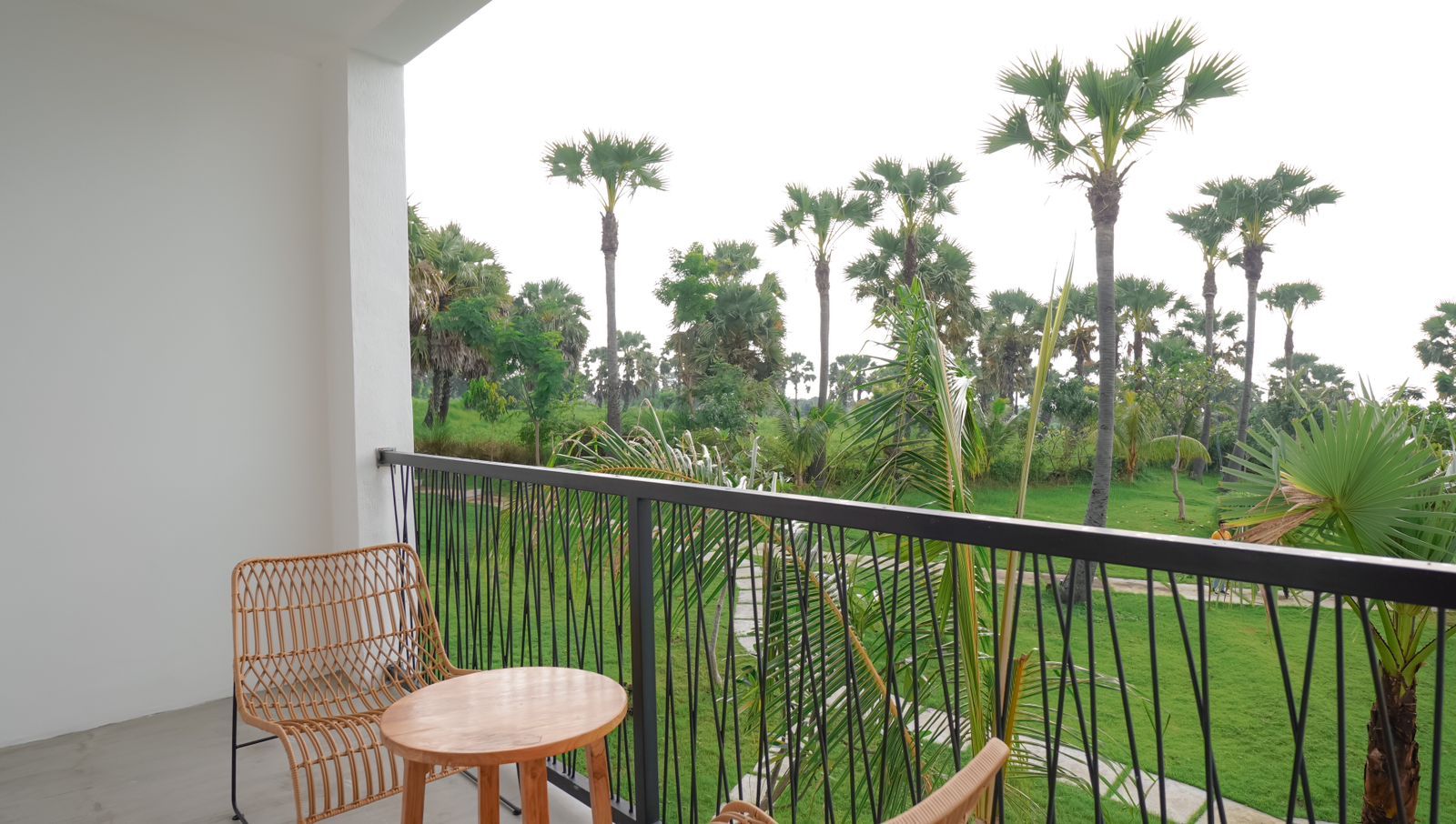 A balcony with a chair and table, overlooking a garden with palm trees.