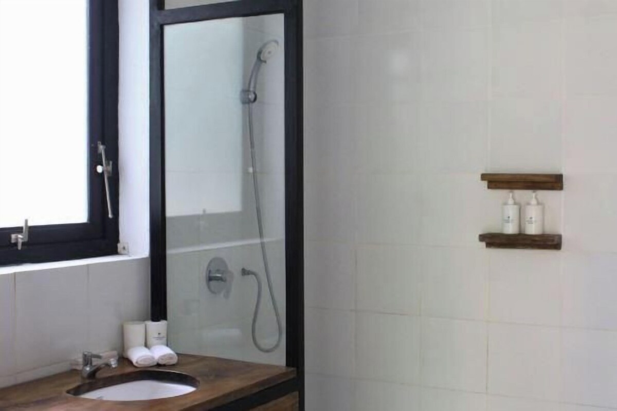 Een badkamer met een douche met glazen wand, een wastafel met spiegel en twee planken met toiletartikelen.