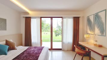 Habitación de hotel con cama, escritorio, silla y puertas de vidrio correderas grandes que dan a un jardín.