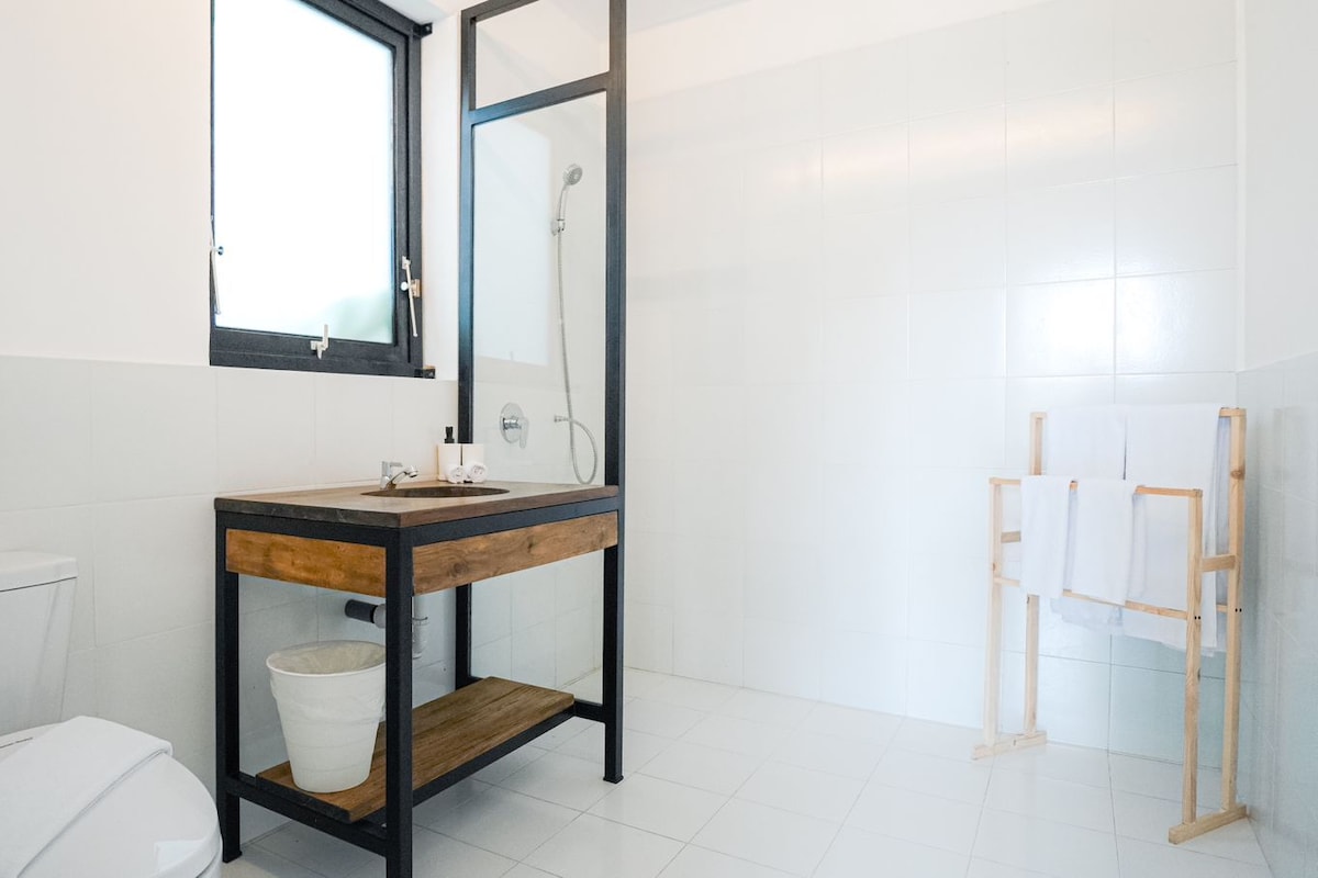 A bathroom with a toilet, sink, shower, and a wooden easel with towels.