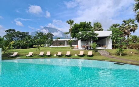 A swimming pool with lounge chairs, a building with a covered area, and a mountain in the background.