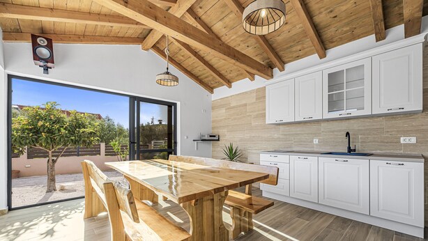 Una cocina moderna con vigas de madera, armarios blancos y una amplia mesa de comedor con bancos.