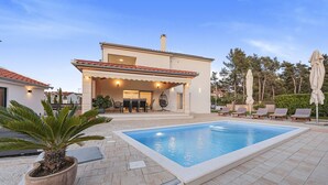 Una casa moderna con piscina, mobiliario de exterior y un jardín cuidado.