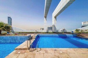 Una piscina en la azotea con agua cristalina azul, un trampolín y vistas a un puente y edificios.