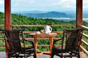 Un balcón con sillas de mimbre y una mesa, con vistas a un paisaje montañoso.
