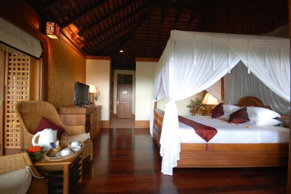 A room with a bed, a chair, a table with a tray of items, and a television.