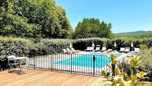 Une terrasse en bois avec une piscine, entourée d’une clôture en métal et de chaises longues.