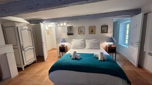 Une chambre à coucher avec un grand lit, deux tables de chevet avec des lampes, une armoire et une porte donnant sur une autre pièce.
